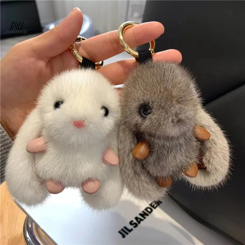 Two fluffy keychains, one white and one gray, held by a hand against a blurred background.