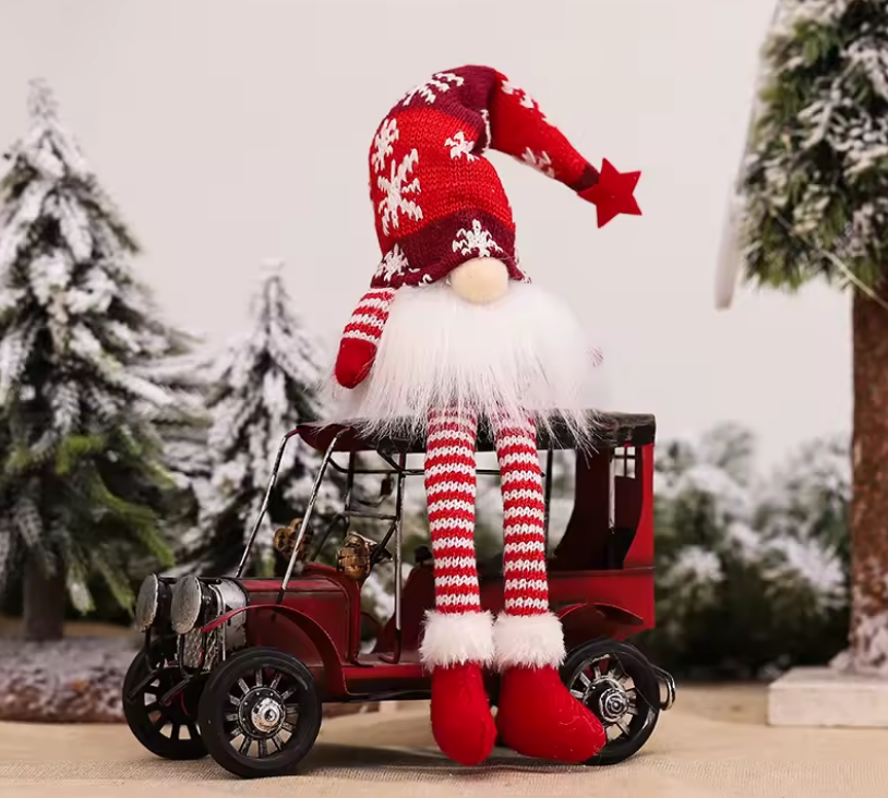 Christmas gnome with a red hat and striped legs sitting on a miniature car with a snowy landscape background.