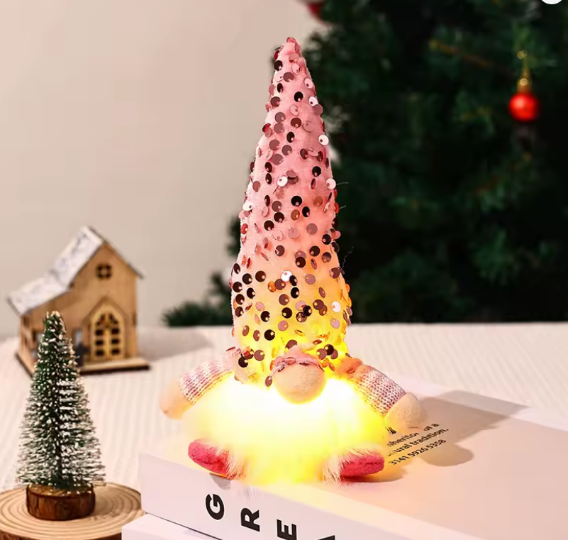 Decorative LED gnome with sequin cone hat on a table with a Christmas tree in the background
