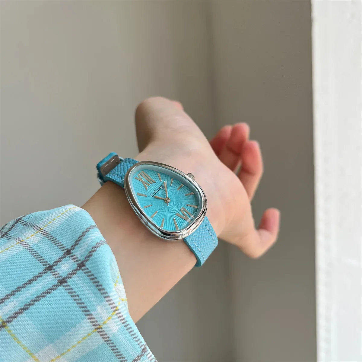 Hand wearing a turquoise watch with a matching turquoise fabric sleeve against a neutral background