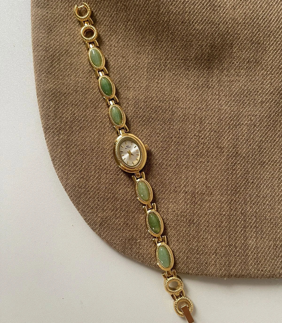 Gold bracelet with green gemstones on a brown fabric background