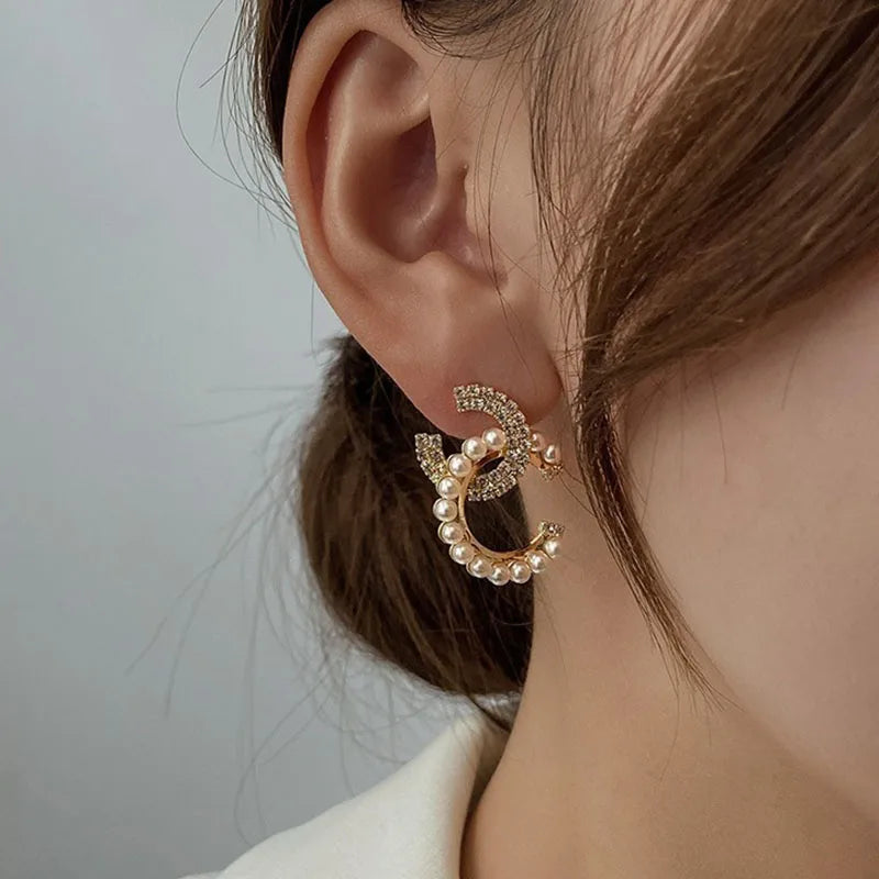 Close-up of an ear wearing a gold and pearl earring against a neutral background