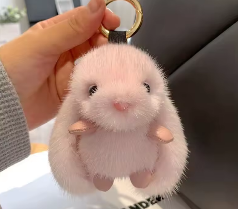 Fluffy white keychain shaped like a hamster held by a hand.
