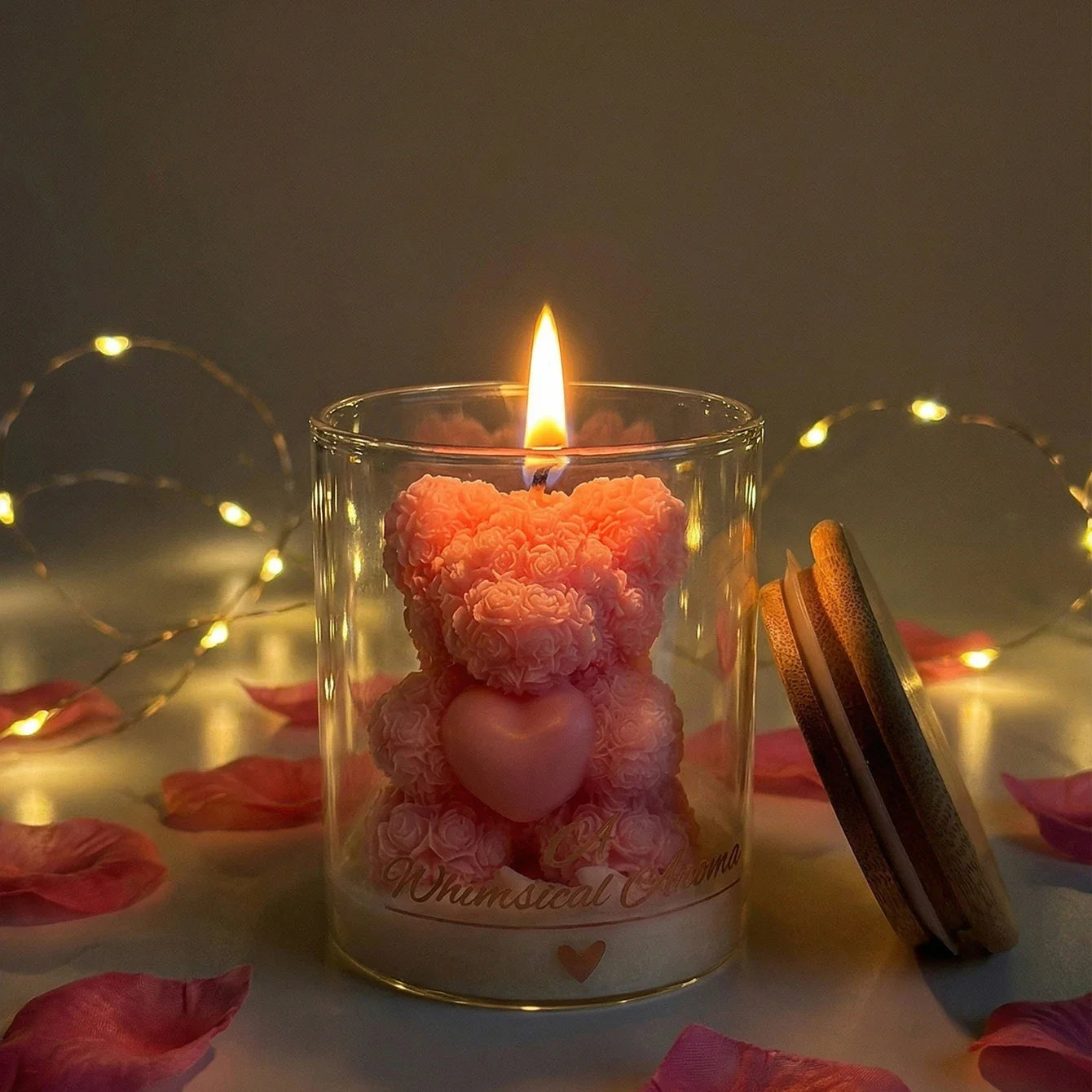 Candle in a glass jar with a pink teddy bear-shaped candle inside, surrounded by fairy lights and rose petals.