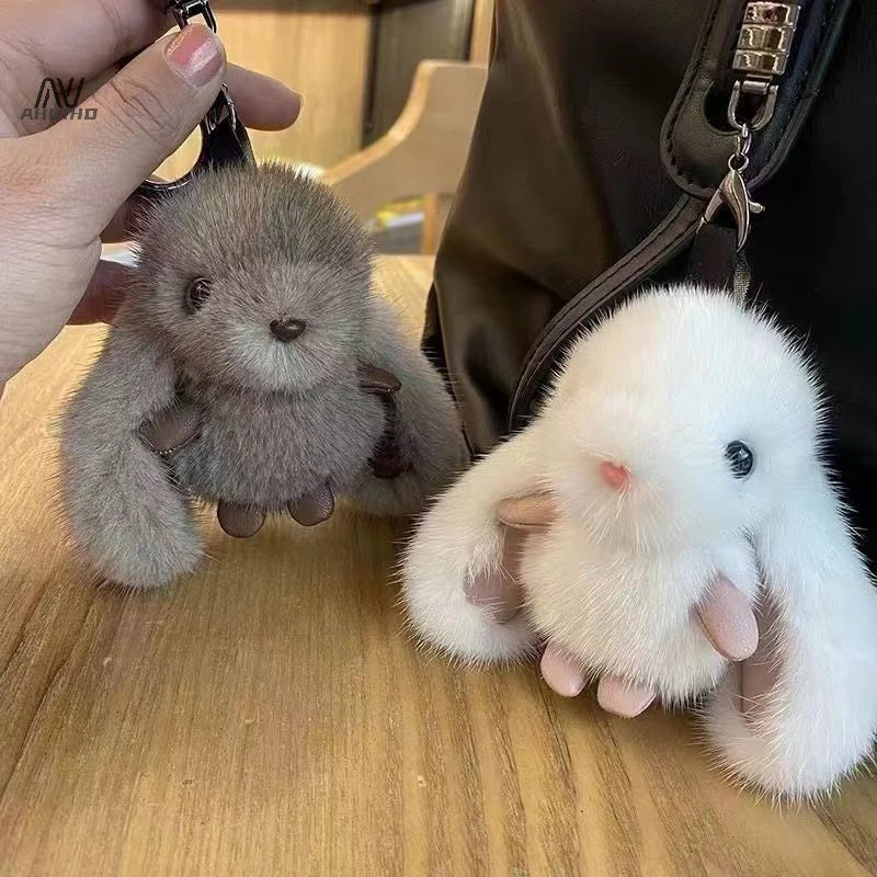 Two plush keychains, one gray and one white, held by a person on a wooden surface.