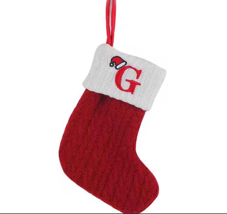 Red knitted Christmas stocking with a white cuff featuring a red 'G' and Santa hat design on a white background.