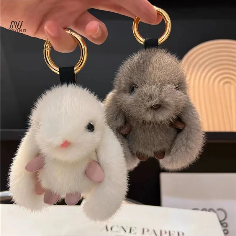 Two fluffy keychains, one white and one gray, held by a hand against a blurred background.