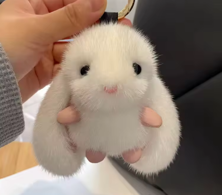 White fluffy keychain shaped like a rabbit held by a hand against a blurred background