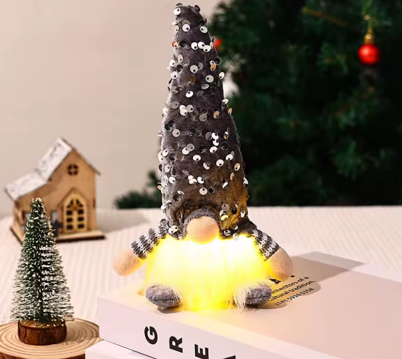 Decorative gnome with sequin hat and LED light on a table with a Christmas tree in the background.