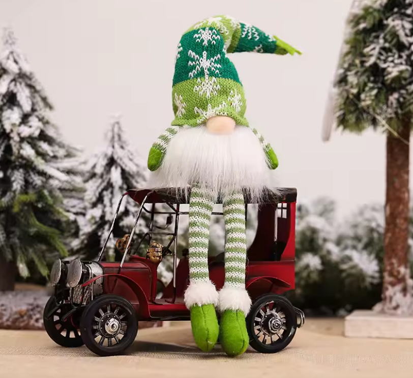 Christmas gnome with a green hat and striped outfit sitting on a small red car with a snowy background.