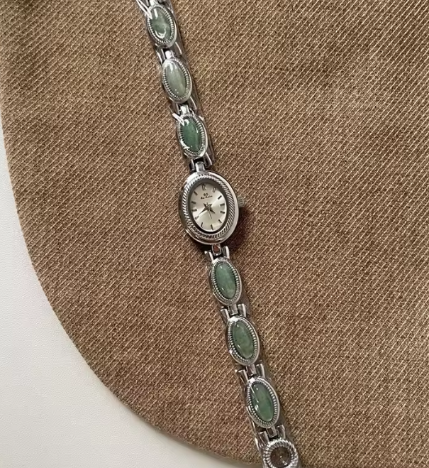 Silver watch with green gemstones on a brown circular stand