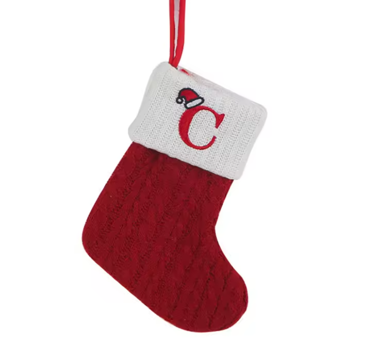 Red Christmas stocking with white cuff featuring a letter 'C' and Santa hat, on a white background.