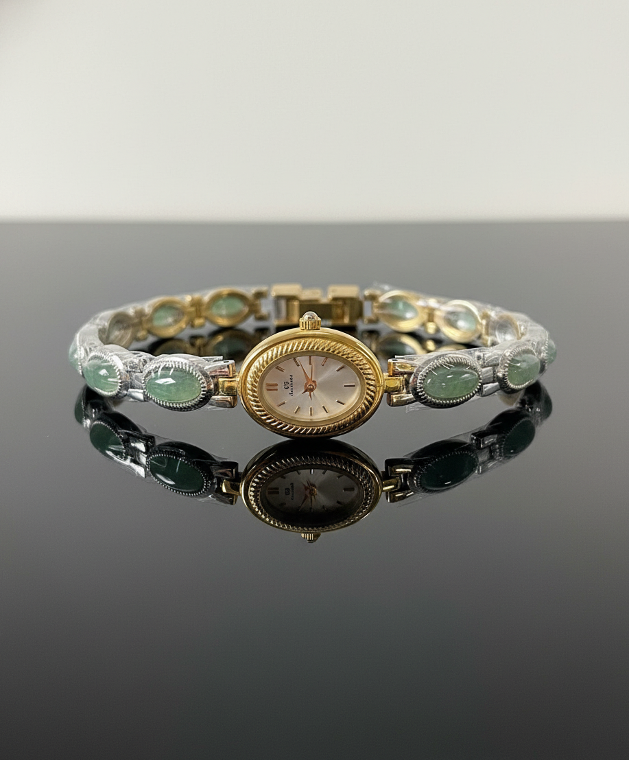 Gold and silver bracelet with green gemstones on a reflective surface
