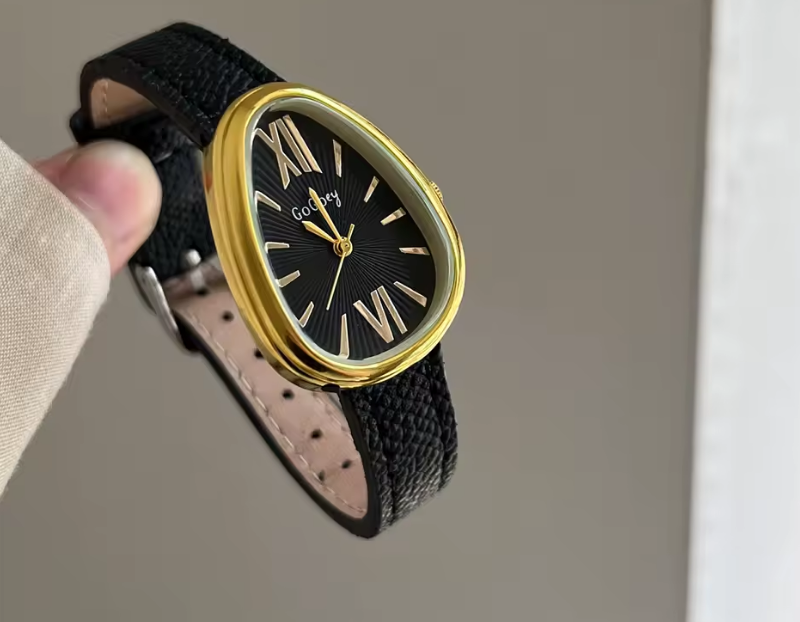 Wristwatch with black strap and gold case held by a hand against a neutral background