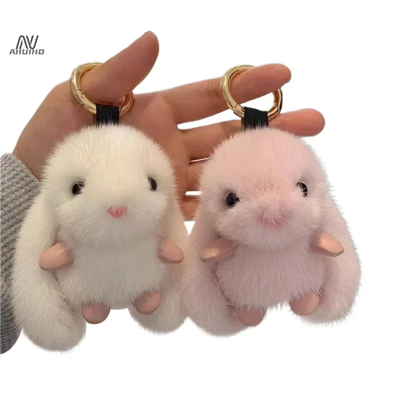 Two fluffy keychains shaped like small animals held by a hand against a white background.